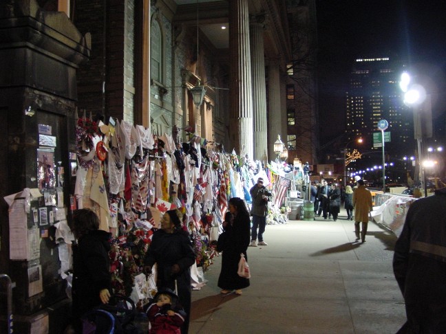 The facade and wrought iron fence around St. Paul’s church at night. The fence is covered papers and cloth banners with messages and well wishes.