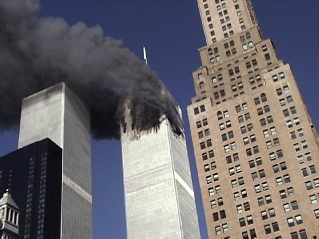Tower 1 of the World Trade Center is ablaze with black smoke eminating from its top.