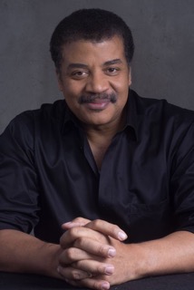 Neil deGrasse Tyson sitting with his hands crossed.