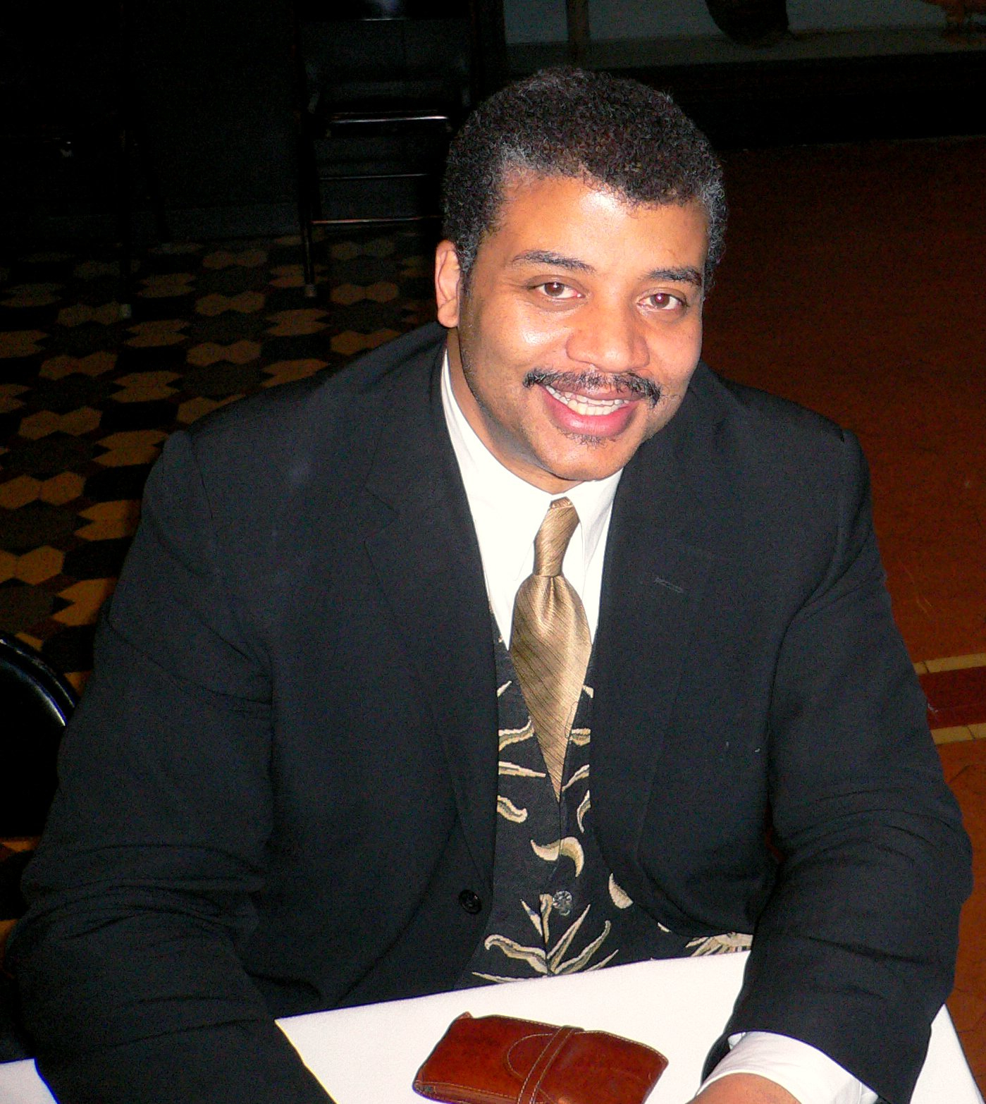 Neil deGrasse Tyson seated signing books after an event at the American Museum of Natural History.