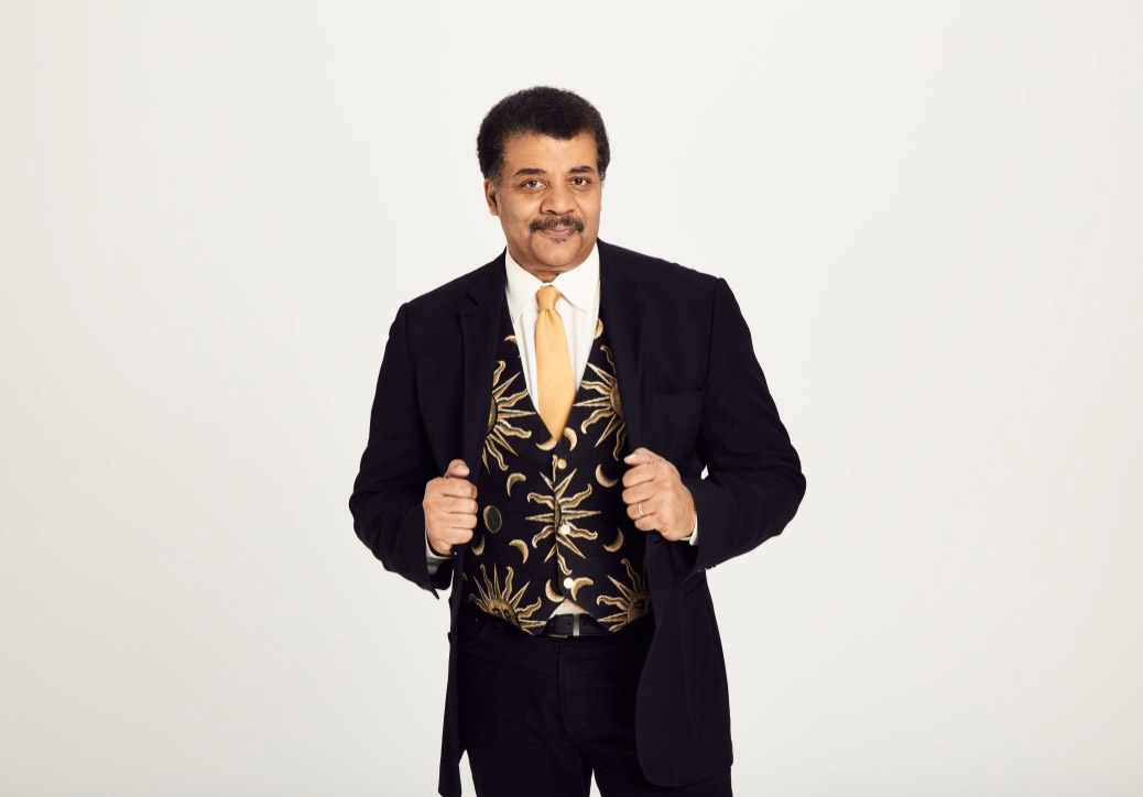 Neil deGrasse Tyson standing holdoing the lapels of his jacket.