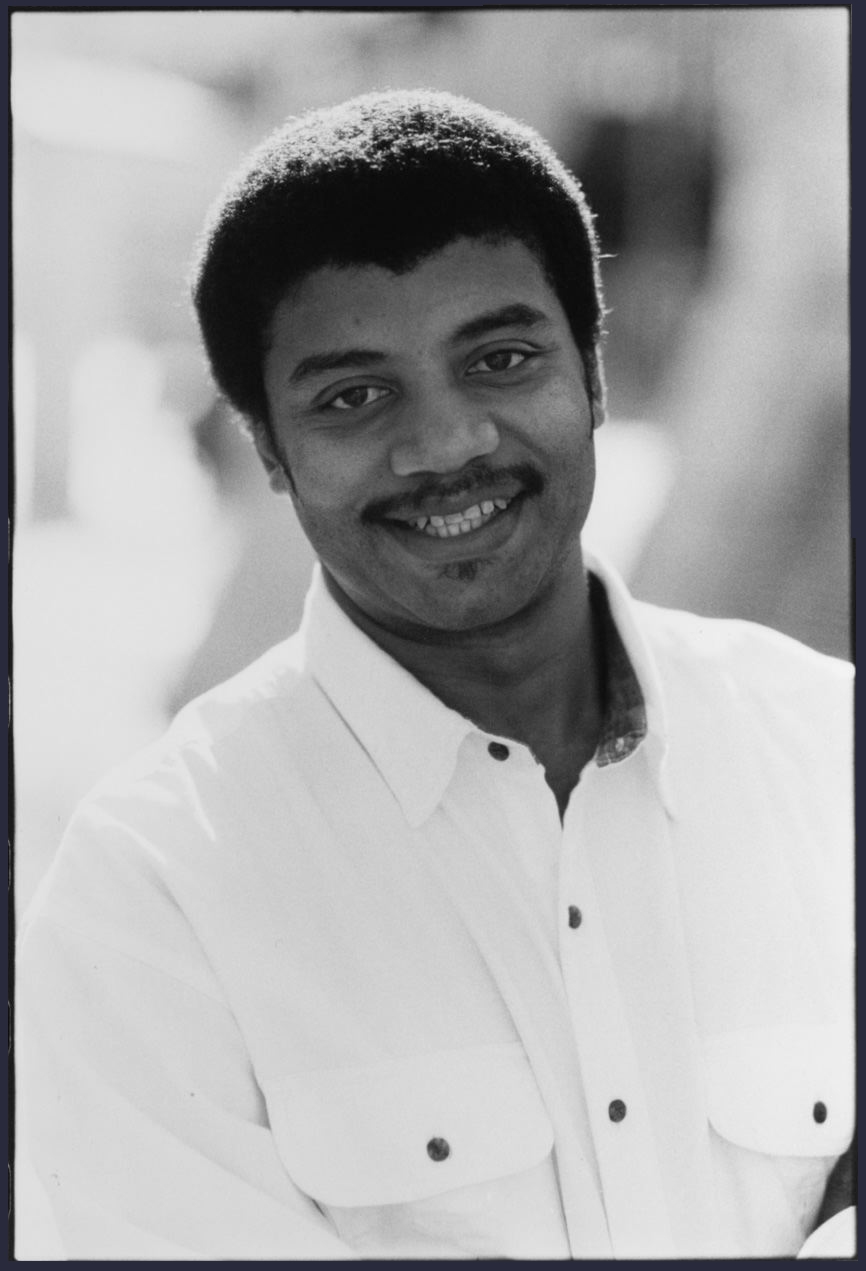 A black and white portrait of Neil deGrasse Tyson with an engaging smile.
