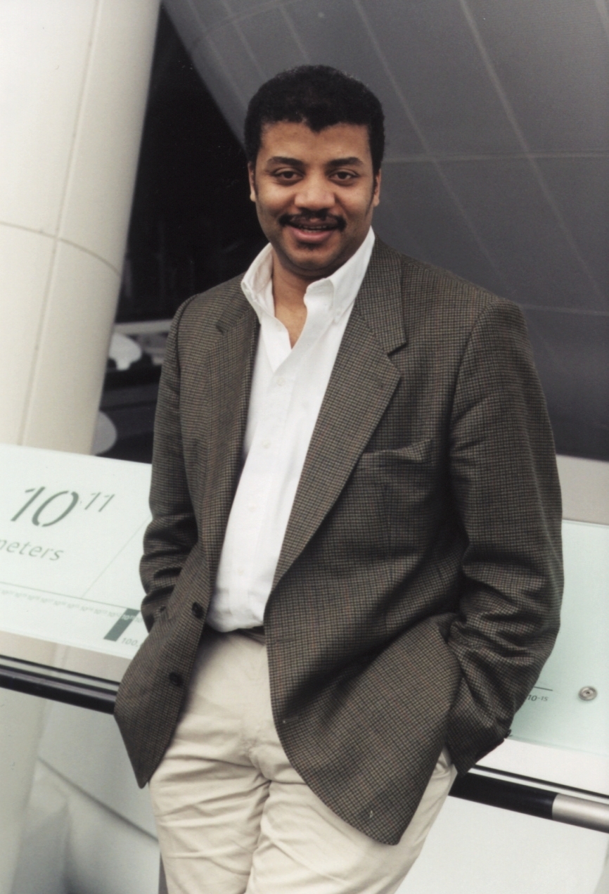 Neil deGrasse Tyson in the Rose Center for Earth and Space, casually pictured in front of the scales of the universe exhibit.