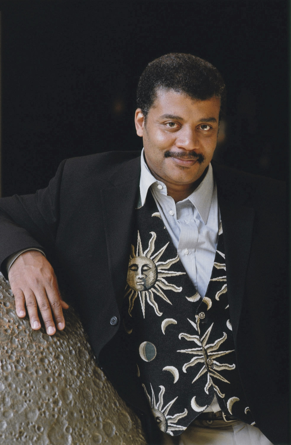 Neil deGrasse Tyson looking into the camera while leaning on the large, three-dimansional model of the Moon.