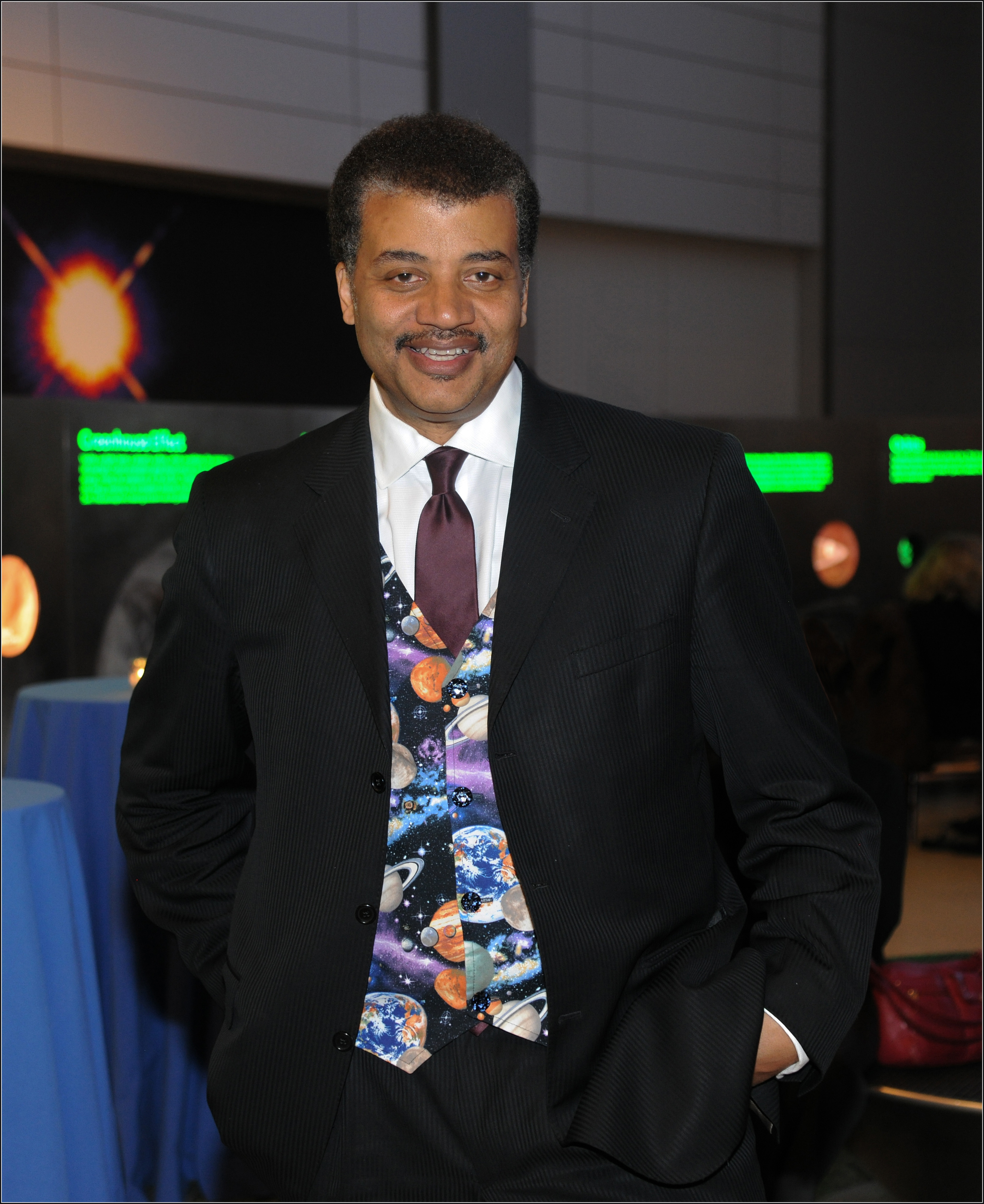 Neil deGrasse Tyson standing in the Hll of the Universe donning his planet vest.