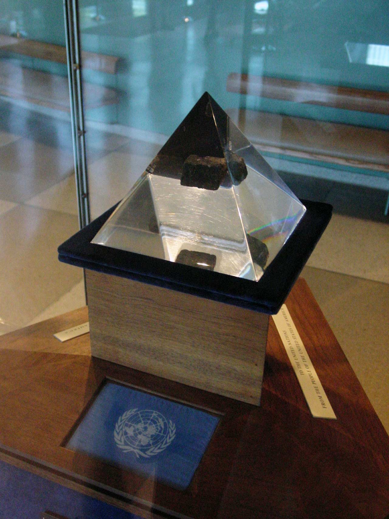 A small Moon rock encased in a pyramid of lucite inside a display case.