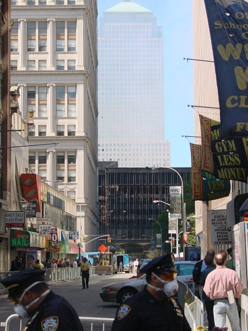 The view toward the site from Fulton Street, with the shattered World Trace Center 5 and the World Financial Center in the background. The sky remains partially filled with dust and smoke.