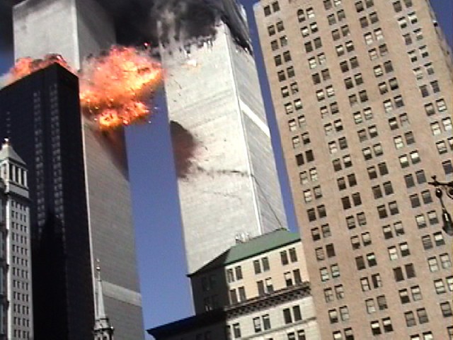 The impact on Tower 2 explodes with smoky plane parts falling to the ground.