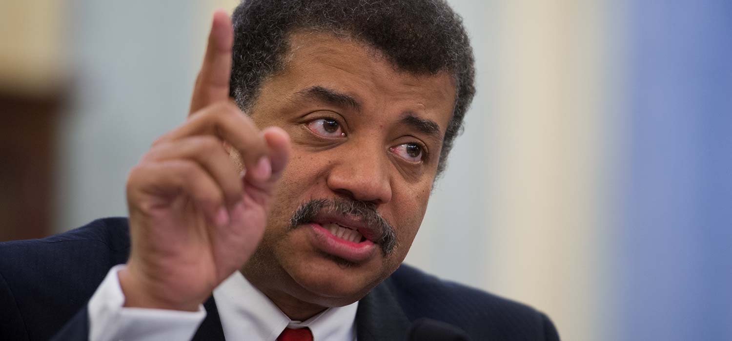 Close up of Neil deGrasse Tyson's face and his hand with his index finger pointing up.