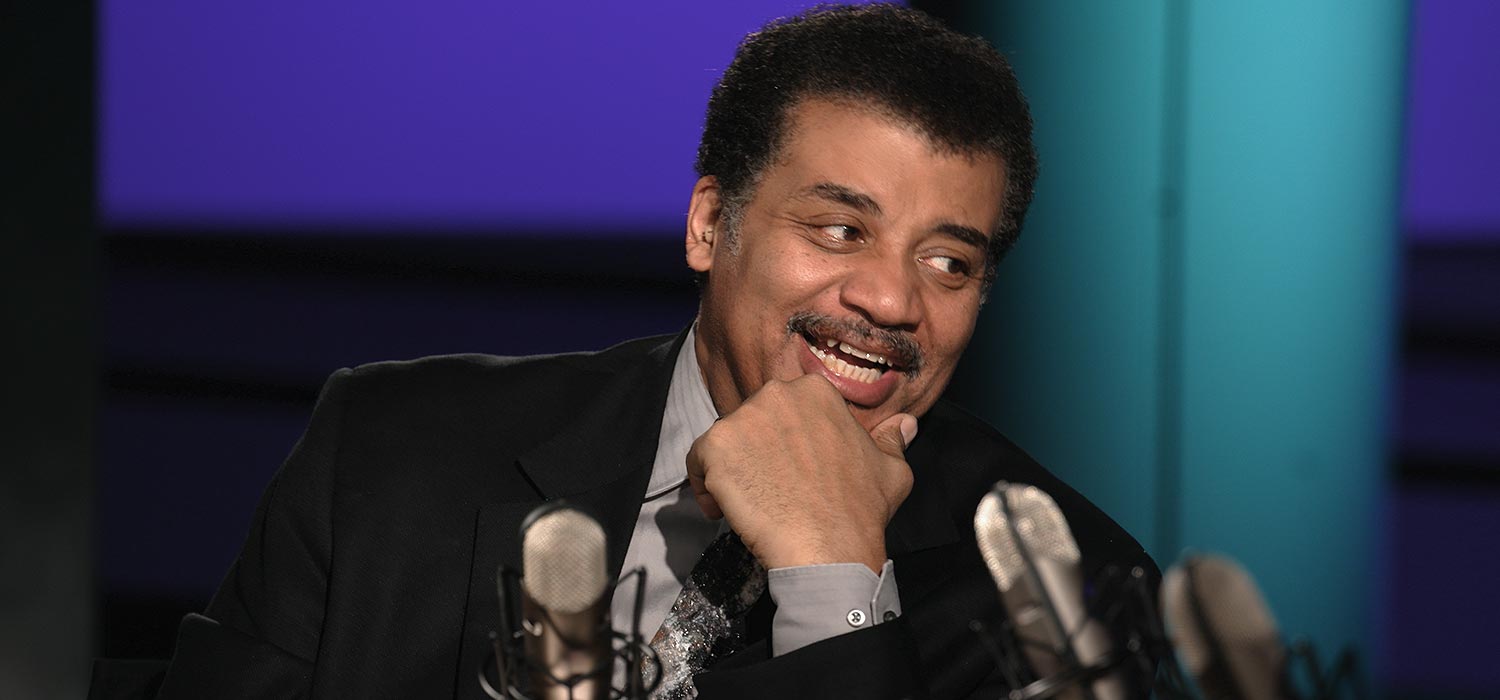 Neil deGrasse Tyson hosting StarTalk, looking over at his guest with a smile.