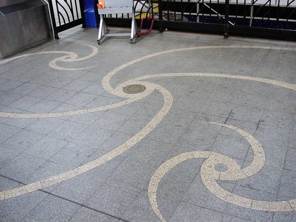 The floor of the subway station with decorative spiral objects in tile that loosely represent spiral galaxies.