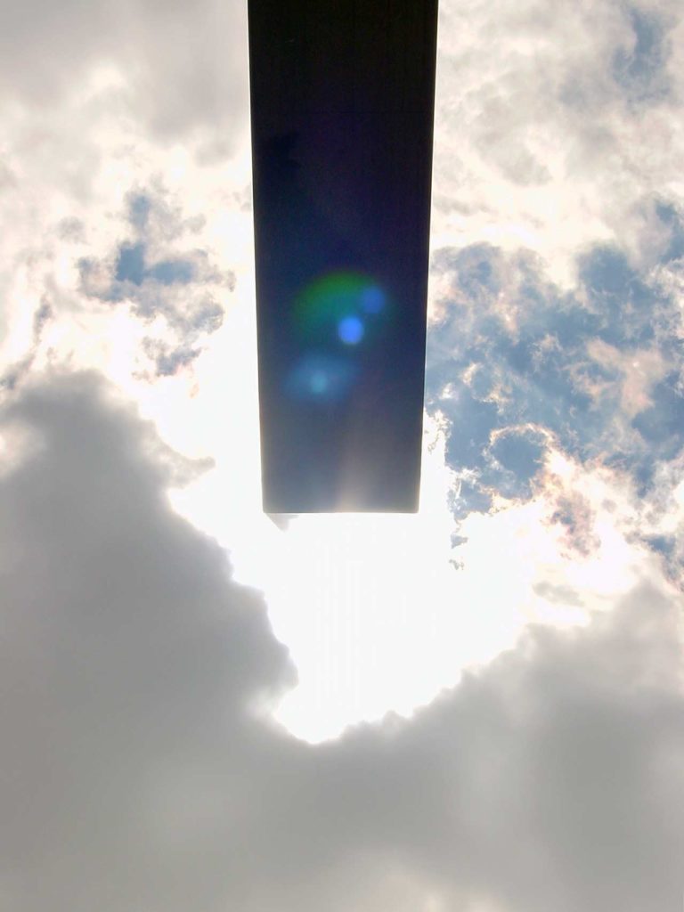 A photo looking up to the sun in a partially cloudy sky, showing the sun in alignment with the short side of the Sun Triangle.