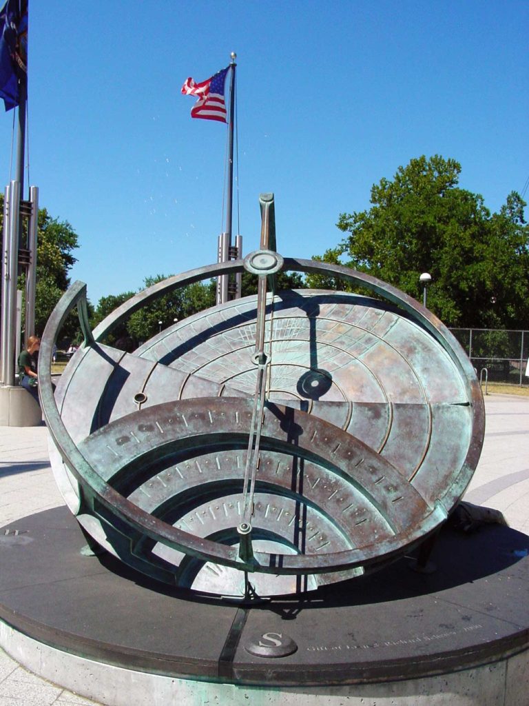 Photo of the elaborate sundial, a large, round, metal sculpture with many levels and the shadow over the time indicators.