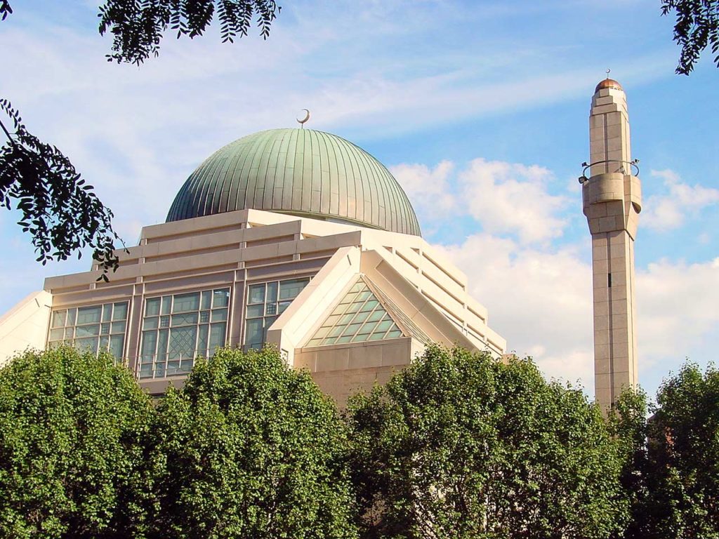A photo of the top of the Islamic Cultural Center above the foreground trees. Ther is a minaret on the right, and a huge domed building with a crescent moon on top.