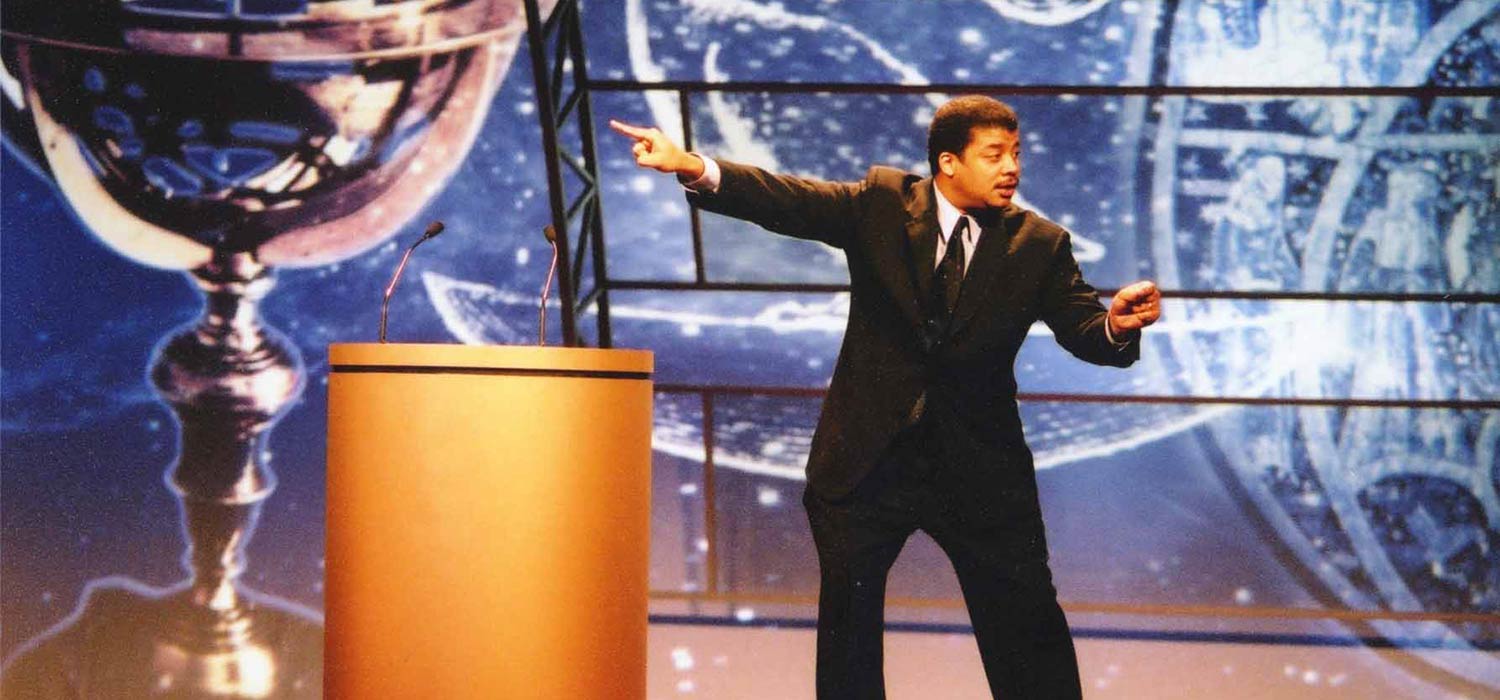 Neil deGrasse Tyson expressively pointing into the air during a speech.