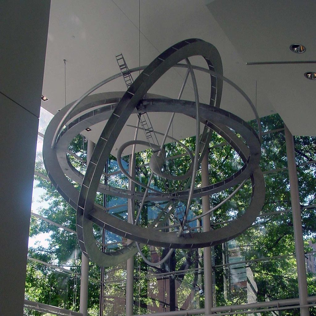 A huge armillary sphere hanging from the ceiling. The steel structure is composed of many rings, and has a spiral galaxy at its center.