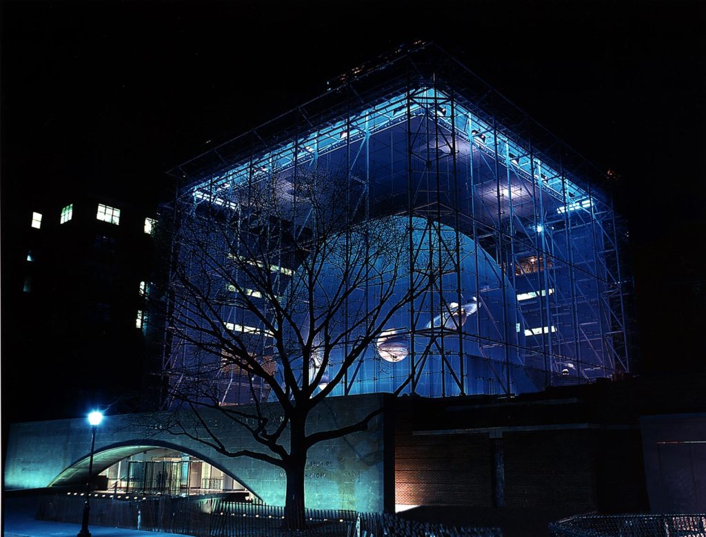 A night shot of the Rose Center for Earth and Space looking at the glass cube, and the sphere illuminated in blue light.
