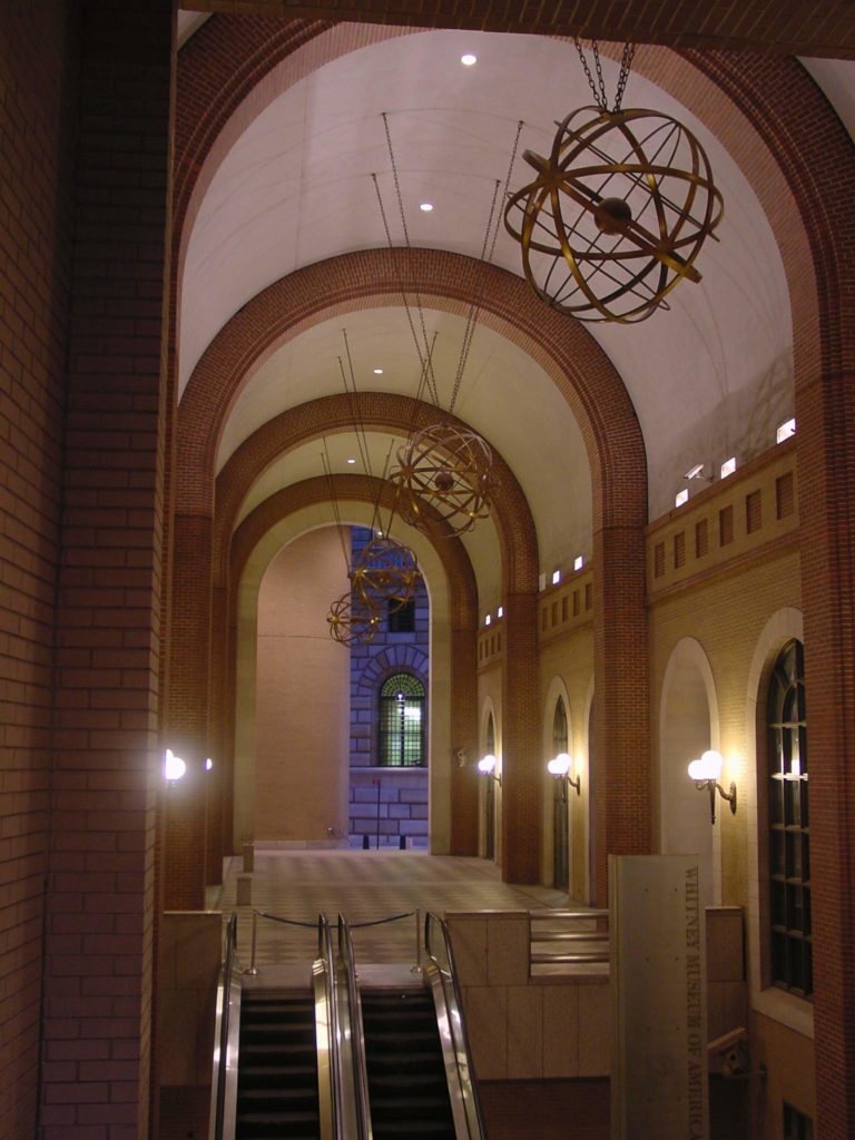 A photo looking through a vaulted arcade in Federal Reserve Plaza and the four armillary spheres hanging from the ceiling.